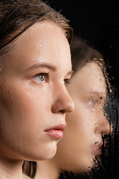 Close up view of fair haired woman with wet skin looking away near blurred mirror on black