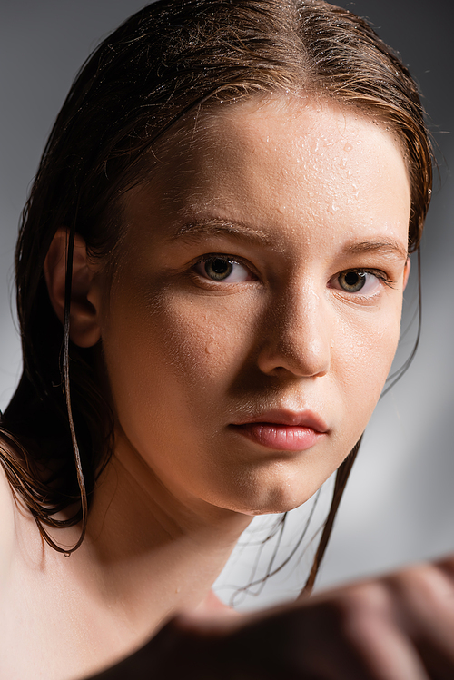 Portrait of young woman with wet skin on face looking at camera on grey background