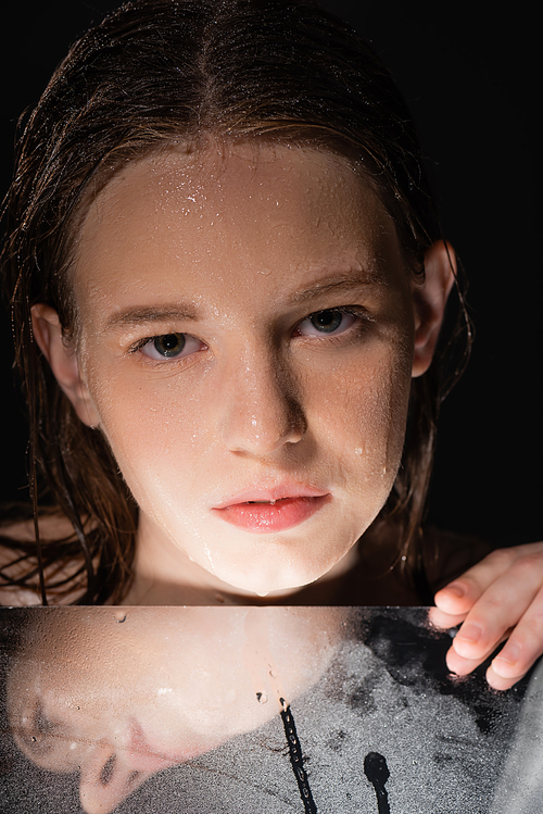Portrait of model with wet face touching mirror isolated on black