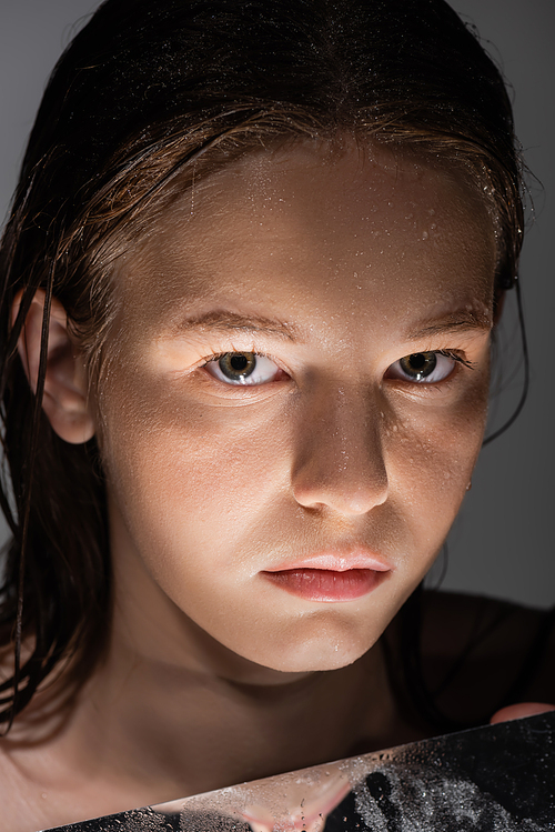 Portrait of woman with wet skin looking at camera near mirror with light isolated on grey