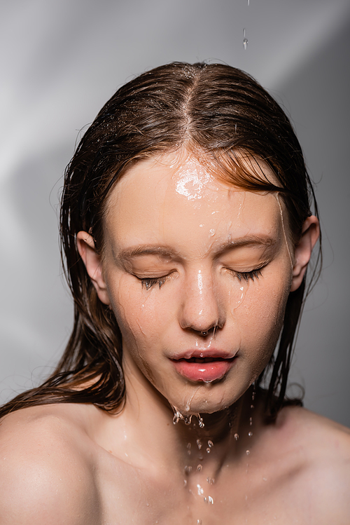 Portrait of young woman with water on skin closing eyes on grey background