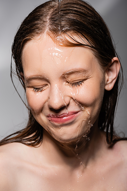 Smiling woman with water on face closing eyes on grey background