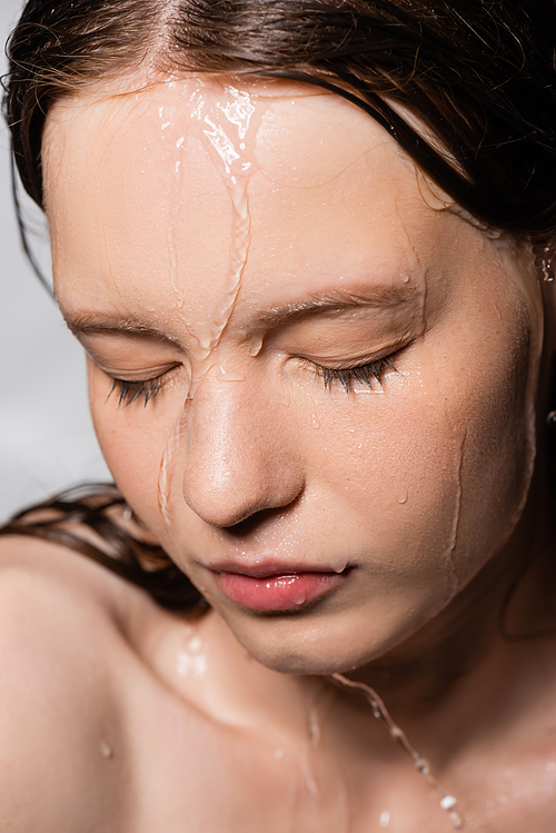 Close up view of water dripping on face of young woman isolated on grey