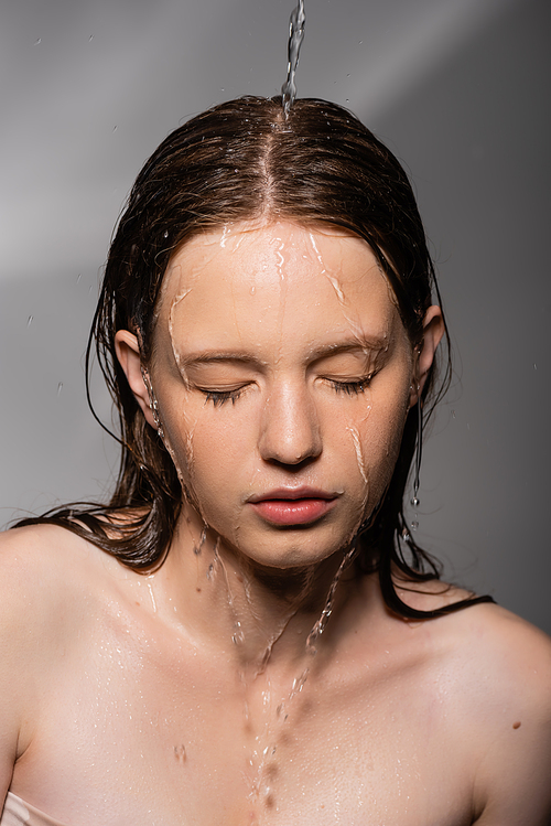 Water pouring on hair and face of young model on grey background