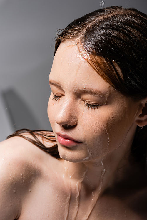 Young woman with water on face and hair on grey background