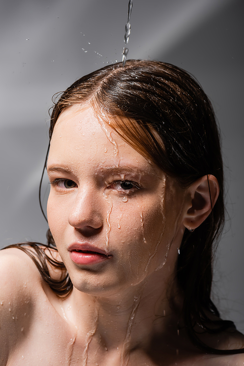 Water pouring on face of young model on abstract grey background