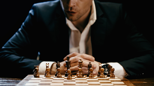 Cropped view of businessman sitting near chess on board isolated on black