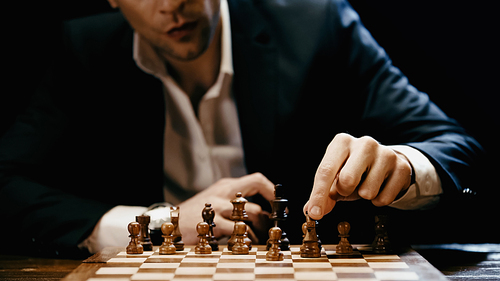 Cropped view of blurred businessman playing chess on table isolated on black