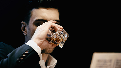 Businessman in formal wear drinking whiskey near blurred newspaper isolated on black