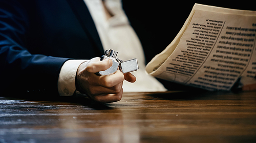 Cropped view of businessman holding lighter and newspaper isolated on black