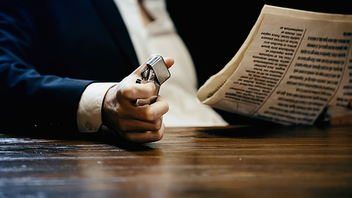 Cropped view of businessman holding lighter near newspaper isolated on black