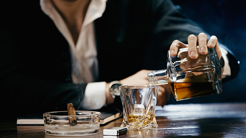 Cropped view of businessman pouring whiskey near cigar and lighter on black