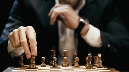 Cropped view of blurred businessman holding chess figure isolated on black