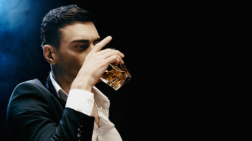 Businessman in formal wear drinking whiskey on black background with smoke