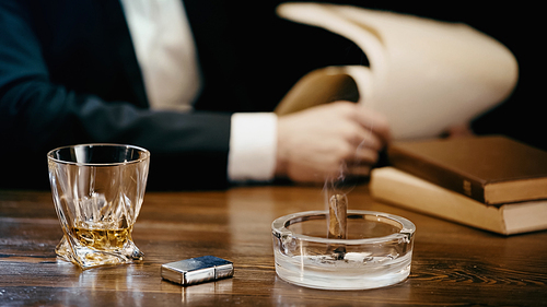Cropped view of cigar and whiskey near blurred businessman isolated on black