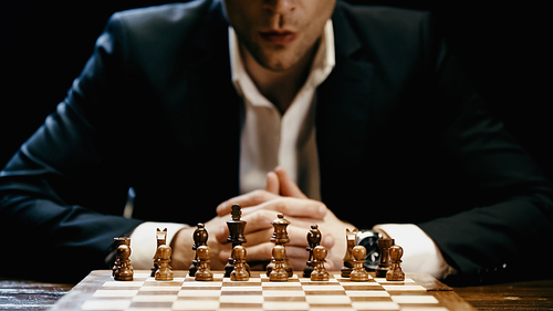 Cropped view of chess on board near blurred businessman in suit isolated on black