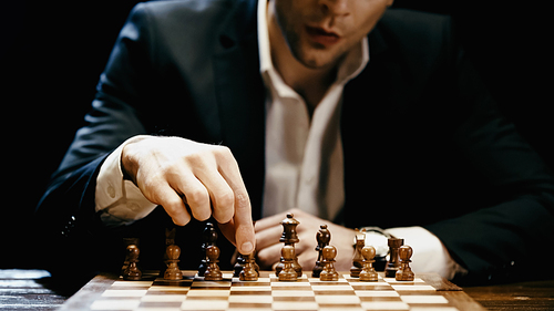 Cropped view of blurred businessman playing chess on table isolated on black