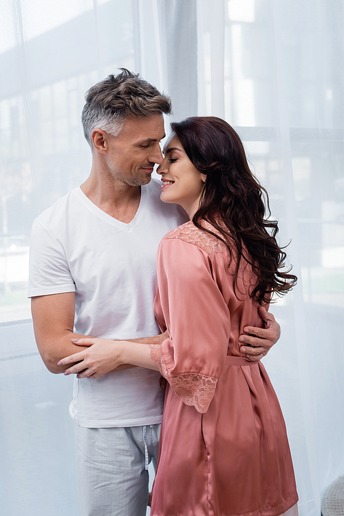 Man in pajamas hugging smiling wife in silk robe at home