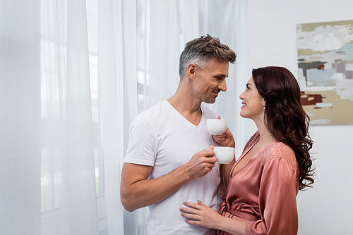 Side view of smiling couple holding cups of coffee at home