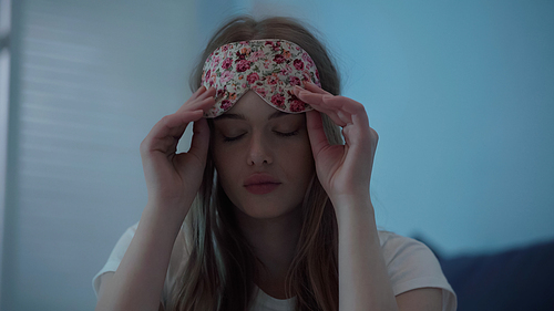 Young woman holding sleep mask at home at night