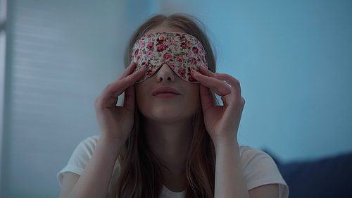 Young woman wearing sleep mask at home at night