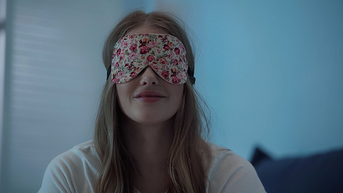 Smiling woman in sleep mask at home at night