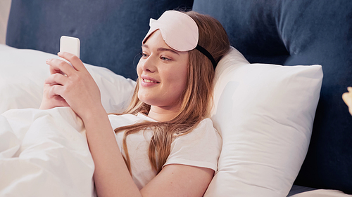 Cheerful woman using smartphone on bed in morning