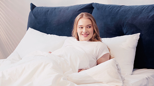 Smiling woman looking away while lying on bed in morning