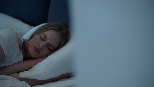 Young woman sleeping on white bedding at night