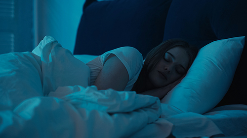 Young woman sleeping on white bedding in bedroom at night