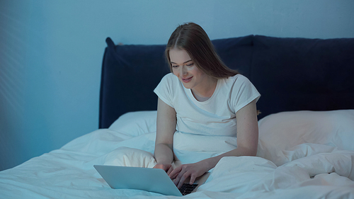 Smiling woman using laptop in bedroom at night