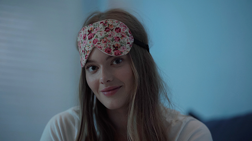 Cheerful woman in sleep mask looking at camera at night