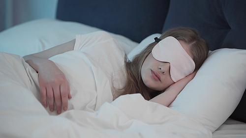 Young woman in sleep mask lying on bed at night