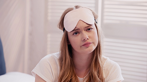 Sad woman in sleep mask looking at camera in bedroom in morning