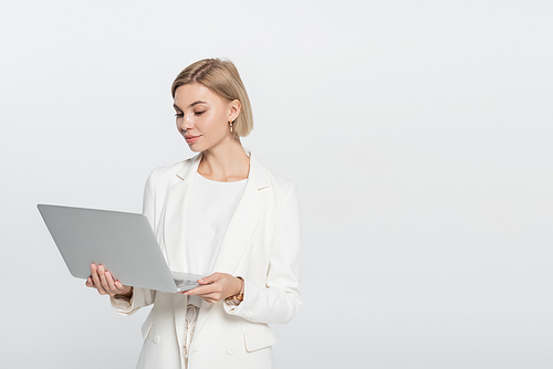 Blonde businesswoman looking at laptop isolated on grey