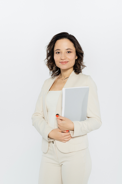 Positive businesswoman in suit holding paper folder isolated on grey