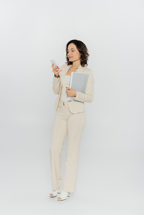 Businesswoman holding paper folder and using smartphone on grey background