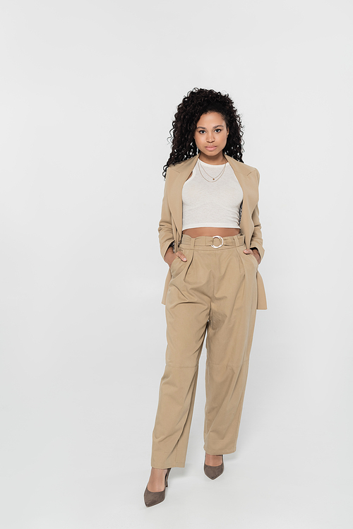 African american businesswoman holding hands in pockets of pants on grey background