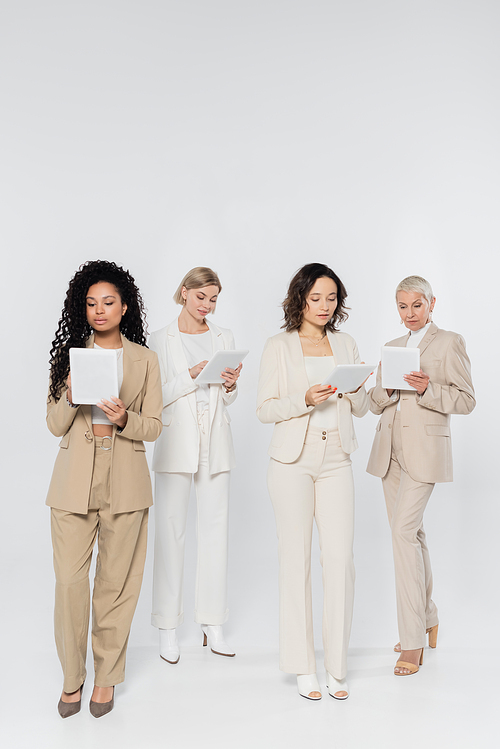 Interracial businesswomen using digital tablets on grey background