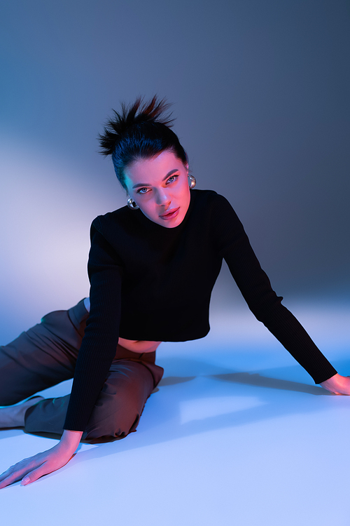 young brunette woman in black sweater and pants looking at camera while posing on blue background