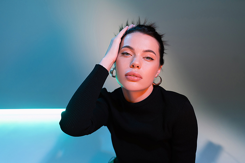 portrait of pretty woman in black sweater touching hair on grey and blue background