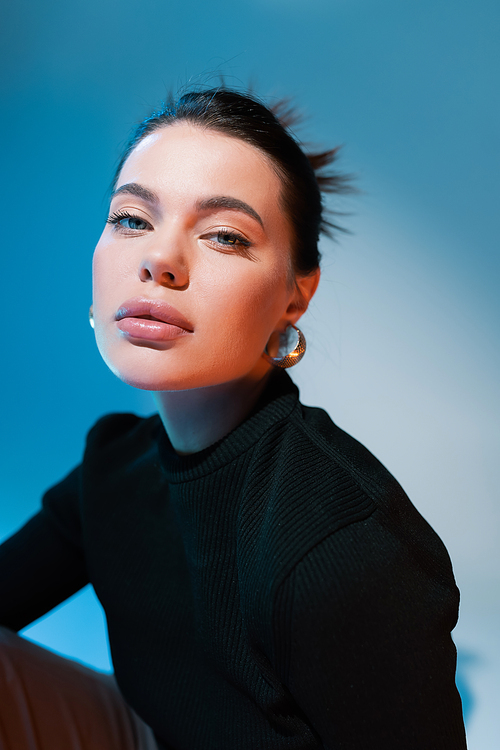 portrait of woman with natural makeup wearing black sweater on blue background