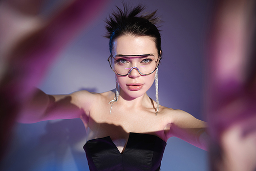 glamour woman in transparent eyeglasses and black corset looking at camera on blurred purple background