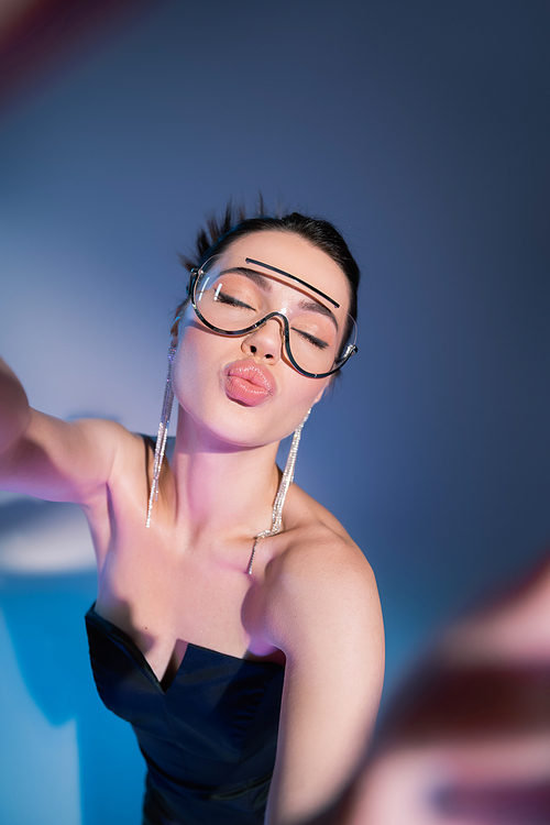 top view of young woman in transparent trendy eyeglasses pouting lips on blue background
