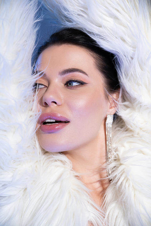 Fashionable woman in faux fur jacket looking away on blue background