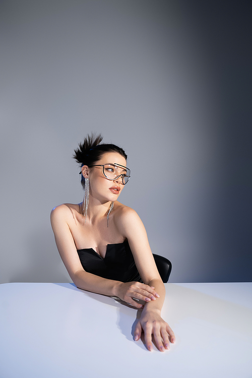 Trendy model in sunglasses and corset posing near table on grey background