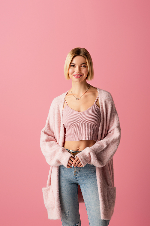 young and happy woman in soft cardigan isolated on pink