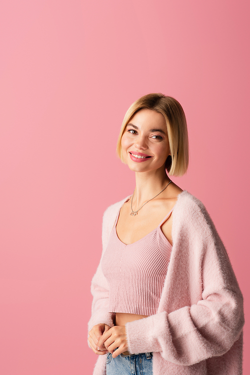 young and positive woman in soft cardigan isolated on pink