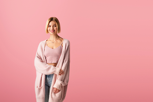 young and pleased woman in soft cardigan isolated on pink