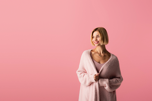 pleased young woman in cardigan isolated on pink